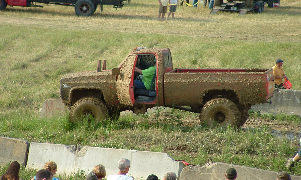 A truck and driver inside covered in mud after a mudding competition.