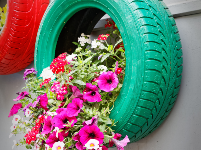 Painted green tire hanging on a wall with pink flowers coming out of it.