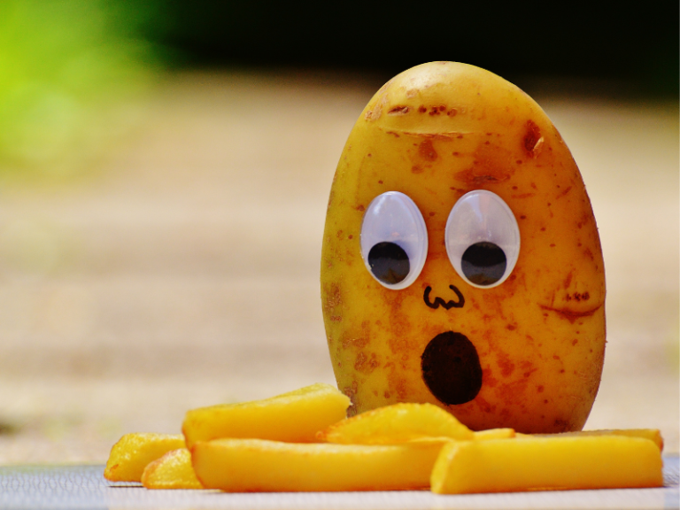 potato with googly eyes looking shocked as it stares down at a few french fries.