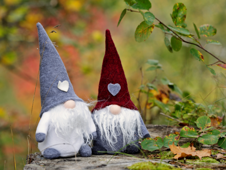 two handmade gnomes sitting on a rock outside.