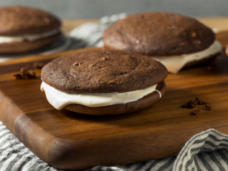 Whoopie pies with icing in the middle laying on a wooden board.